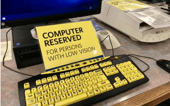 keyboard with bright yellow keys and big characters on them, with a sign saying this computer is reserved for people with low vision
