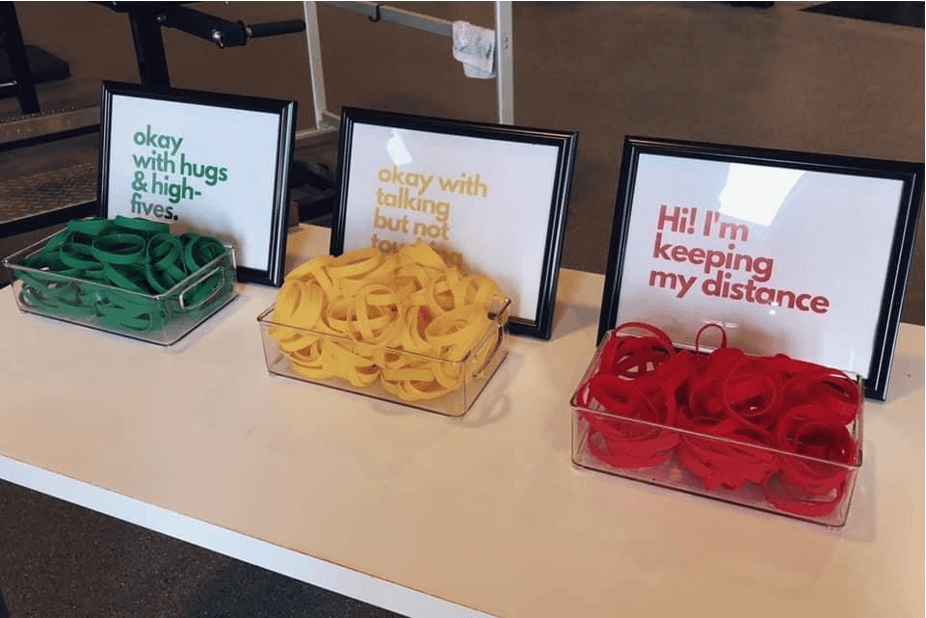 3 boxes of elastic bands with a sign each, for the green ones the sign says ok with hugs, the orange box sign on says ok talking but no touching and the red box sign says I'm keeping my distance